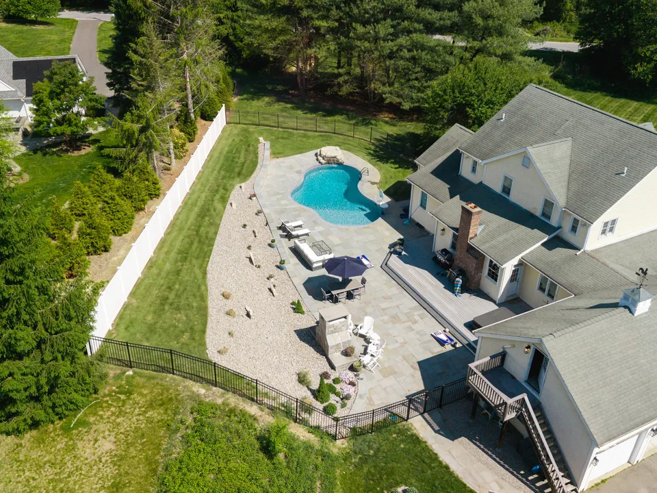 Aerial — the same yard finished: bluestone patio, freeform pool and boulder waterfall — Exterior Services LLC, Newtown, CT