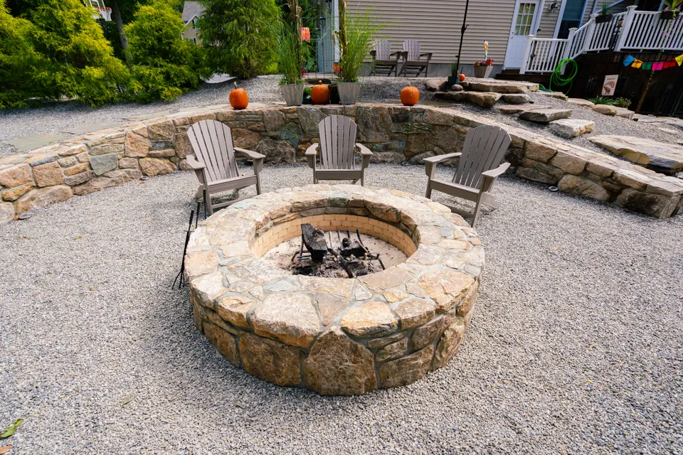 Fieldstone fire pit ring burning, ringed by chairs and a curved stone seat wall — Exterior Services LLC