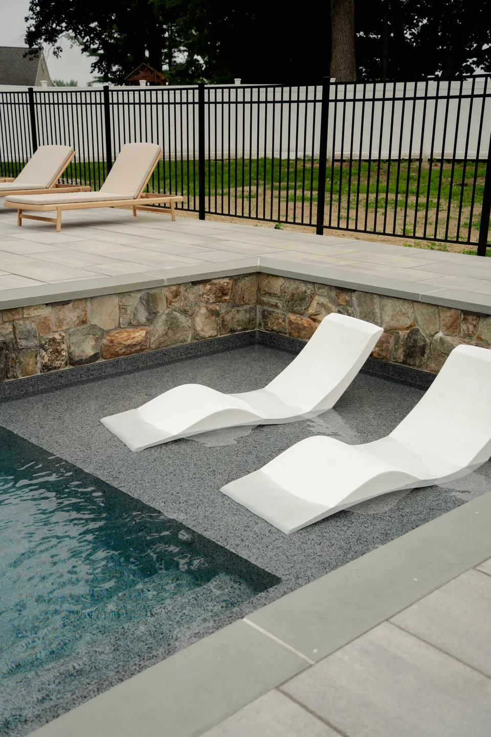 Sun shelf with in-pool chaises against the stone spa wall — Exterior Services LLC, Brookfield, CT
